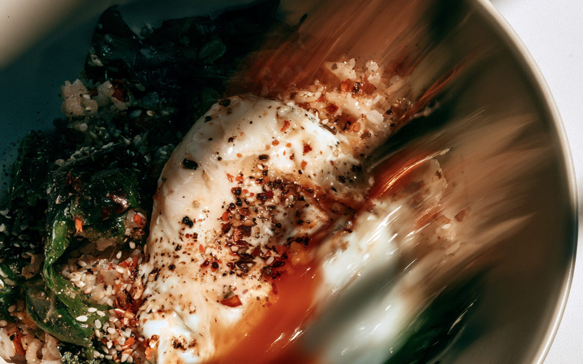 A white bowl of rice with a soft-boiled egg and greens