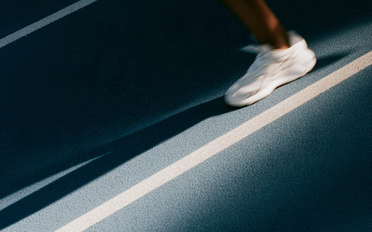 A runner's foot striking a pale blue running track in bright sun