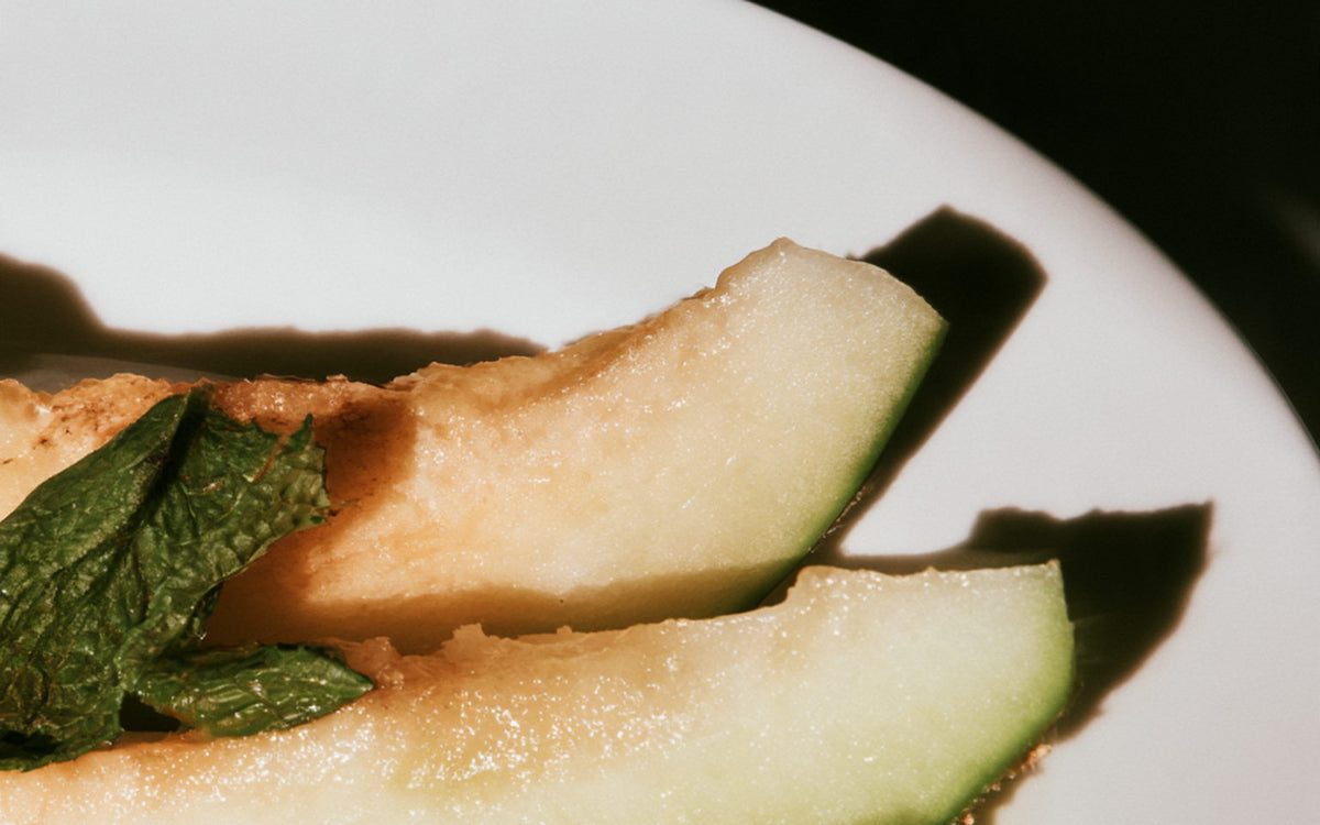 A white plate with sliced pale melon and mint leaves
