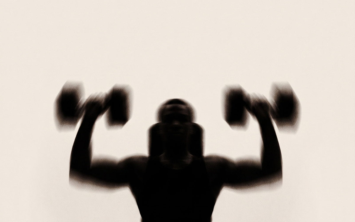 A seated figure pressing two dumbbells overhead, silhouetted against a cream wall