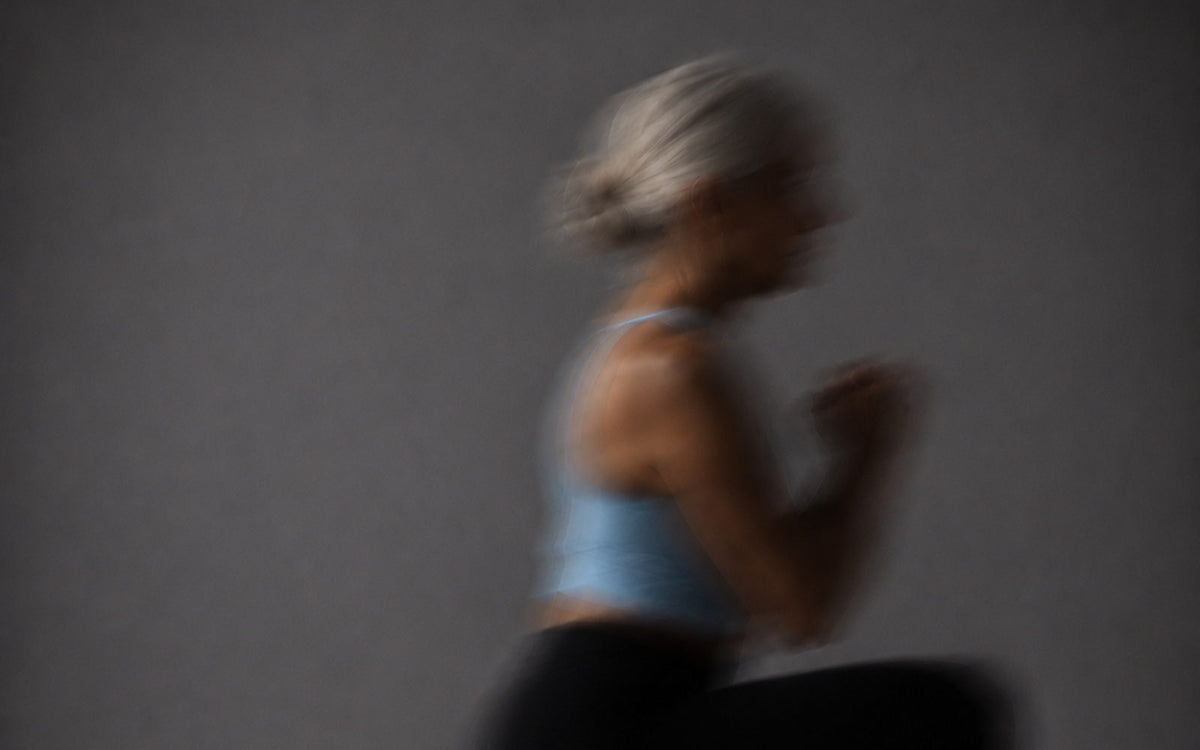 A grey-haired woman mid-lunge, motion-blurred against a grey wall