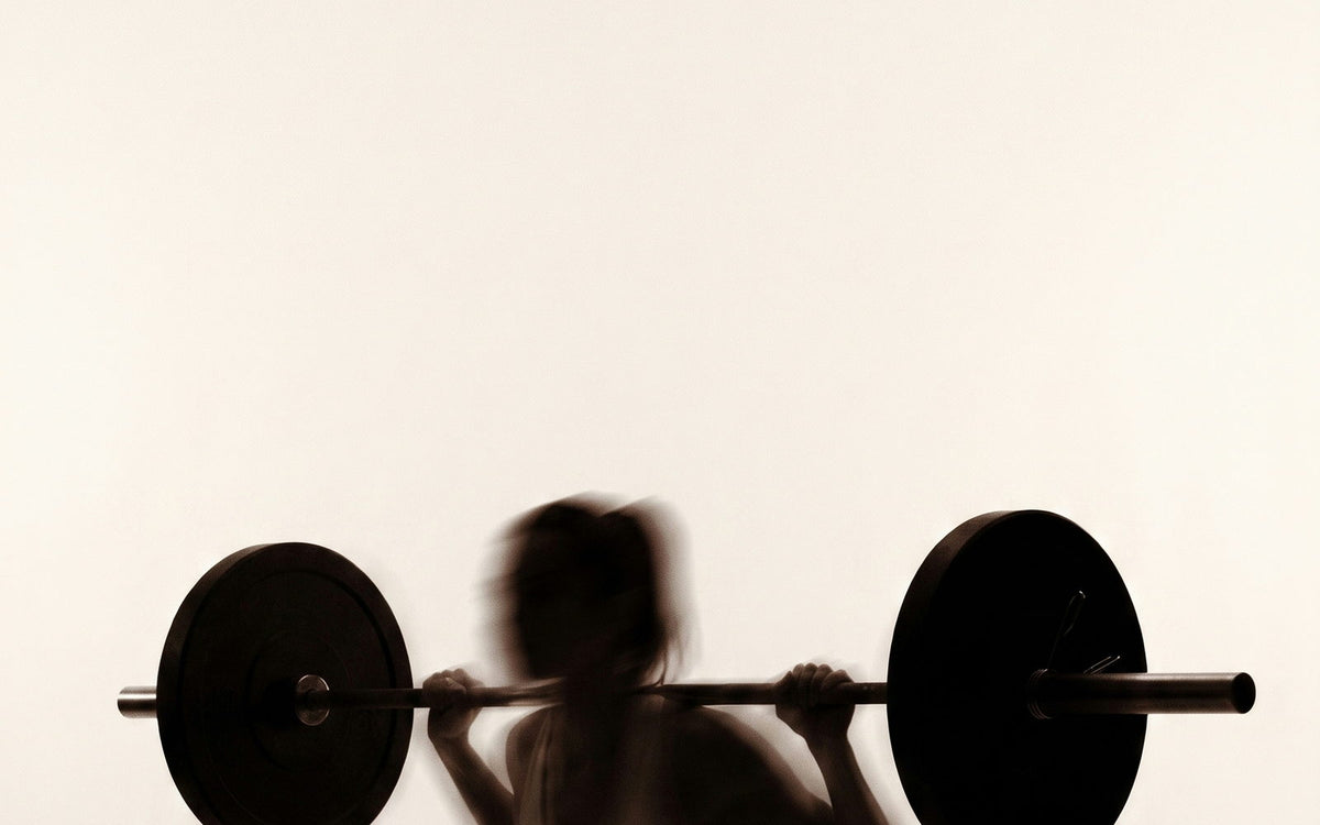 A lifter at the bottom of a barbell squat, motion-blurred against a cream wall